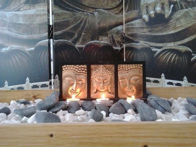Imagem de um ambiente tranquilo com três velas acesas e esculturas de rostos de Buda ladeados por pedras decorativas. O cenário remete à serenidade e à reflexão, ideal para práticas que promovem a consciência e a mudança interna. Este espaço simboliza o despertar da mente e o equilíbrio emocional que a psicoterapia procura alcançar.